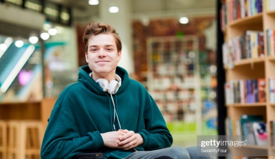 Figura: imagem de jovem cadeirante em uma biblioteca com um headfone sobre o pescoço.